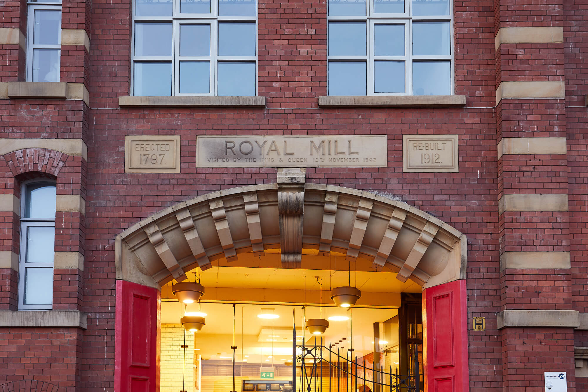 External view of the entrance to Royal Mills showing the red double doors and lights on in the entrance